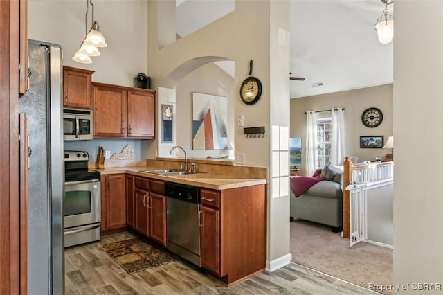 kitchen featuring pendant lighting, sink, a high ceiling, stainless steel appliances, and light wood-type flooring