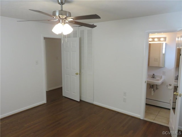 unfurnished bedroom with ensuite bath, a baseboard radiator, dark hardwood / wood-style floors, a closet, and ceiling fan