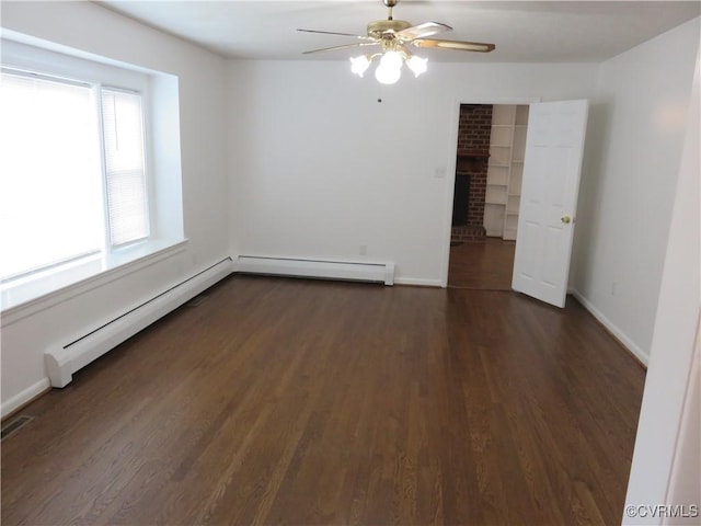 empty room with a baseboard heating unit, dark hardwood / wood-style floors, a brick fireplace, and ceiling fan