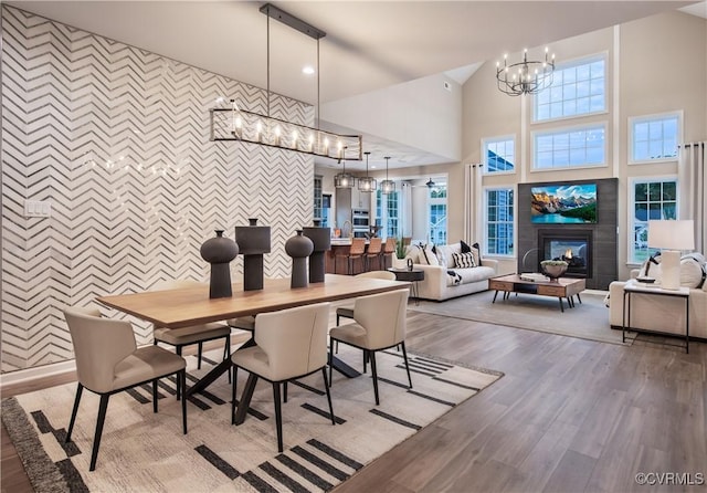 dining space with a tile fireplace, tile walls, a chandelier, hardwood / wood-style flooring, and a high ceiling