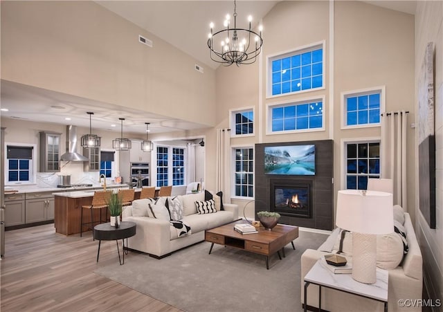 living room featuring a tile fireplace, high vaulted ceiling, an inviting chandelier, and light hardwood / wood-style flooring