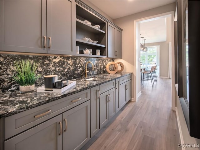 bar with gray cabinets, tasteful backsplash, dark stone countertops, and light hardwood / wood-style flooring