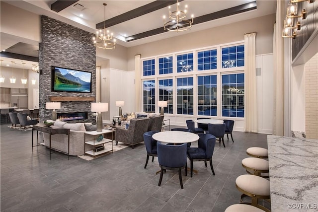 dining room featuring a towering ceiling, a stone fireplace, a chandelier, and beam ceiling