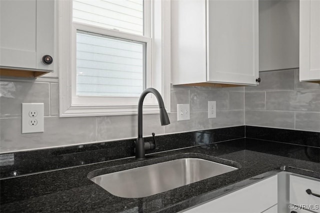 interior details with white cabinetry, sink, backsplash, and dark stone countertops