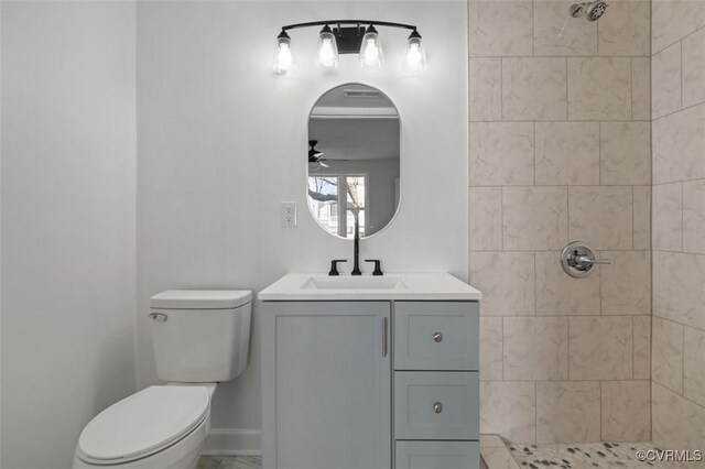 bathroom with ceiling fan, tiled shower, vanity, and toilet