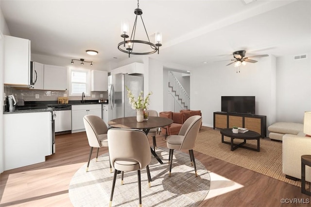 dining space featuring light wood-type flooring, visible vents, ceiling fan with notable chandelier, and stairway