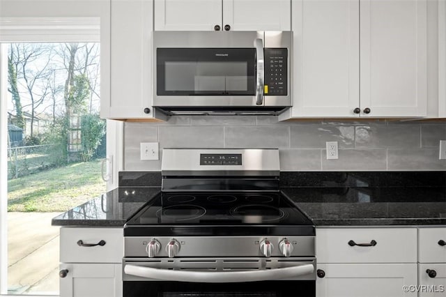 kitchen with stainless steel appliances, white cabinetry, dark stone countertops, and backsplash