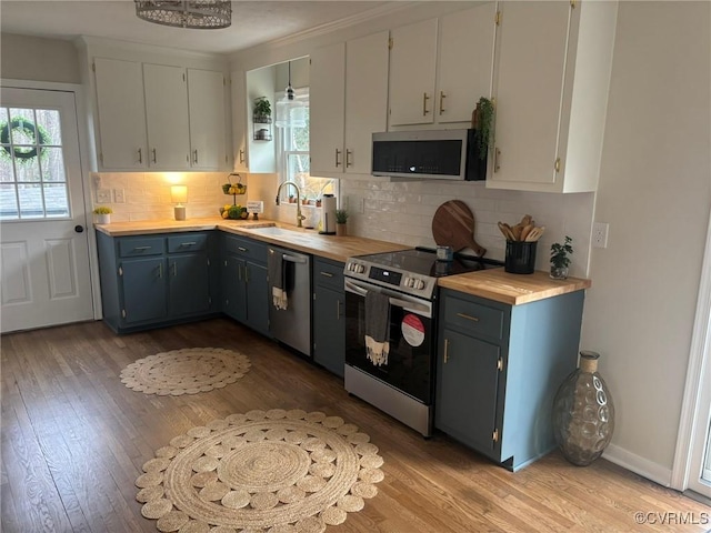 kitchen with appliances with stainless steel finishes, butcher block counters, sink, white cabinets, and backsplash