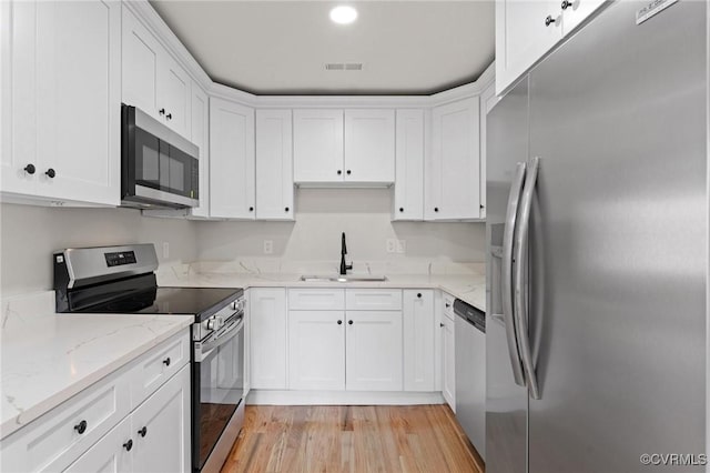 kitchen featuring sink, appliances with stainless steel finishes, white cabinetry, light stone counters, and light wood-type flooring