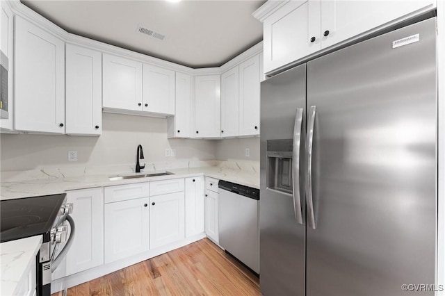 kitchen featuring sink, white cabinetry, stainless steel appliances, light hardwood / wood-style floors, and light stone countertops