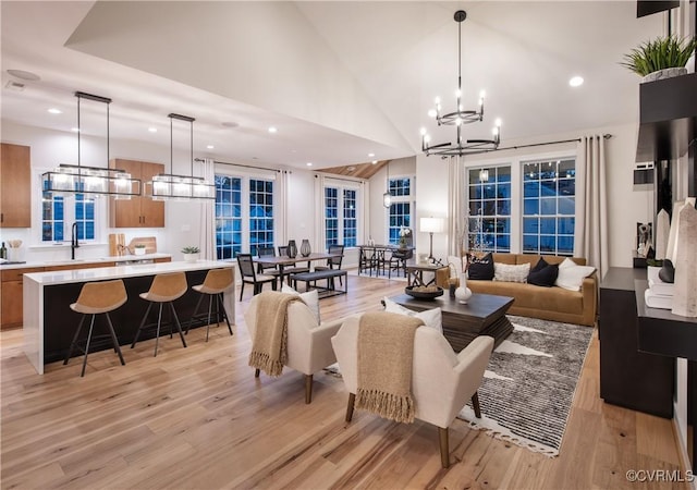 living room featuring high vaulted ceiling, sink, a chandelier, and light hardwood / wood-style floors