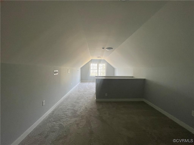 additional living space with dark colored carpet and vaulted ceiling