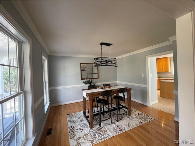 dining space with crown molding, light hardwood / wood-style floors, and a notable chandelier