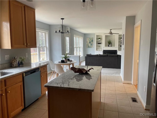 kitchen featuring light tile patterned floors, hanging light fixtures, a center island, light stone counters, and stainless steel dishwasher