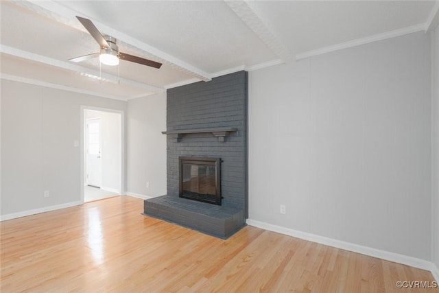 unfurnished living room featuring crown molding, light hardwood / wood-style flooring, ceiling fan, a brick fireplace, and beamed ceiling