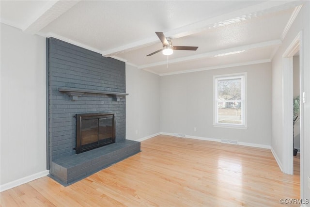 unfurnished living room featuring beamed ceiling, ceiling fan, a brick fireplace, and light hardwood / wood-style flooring