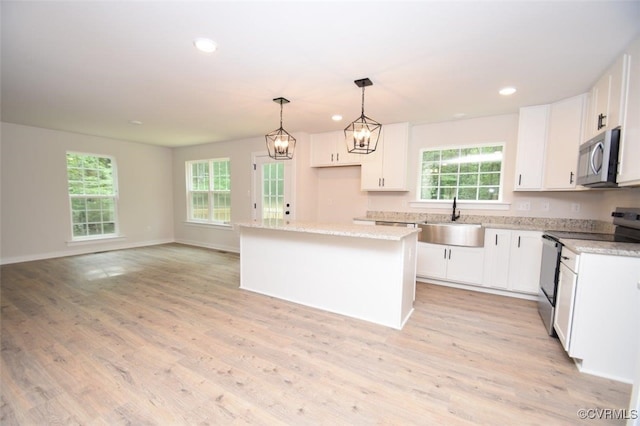 kitchen featuring a healthy amount of sunlight, a center island, electric range oven, a sink, and stainless steel microwave