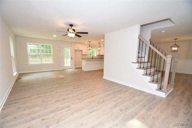 unfurnished living room featuring baseboards, light wood-style flooring, and ceiling fan with notable chandelier