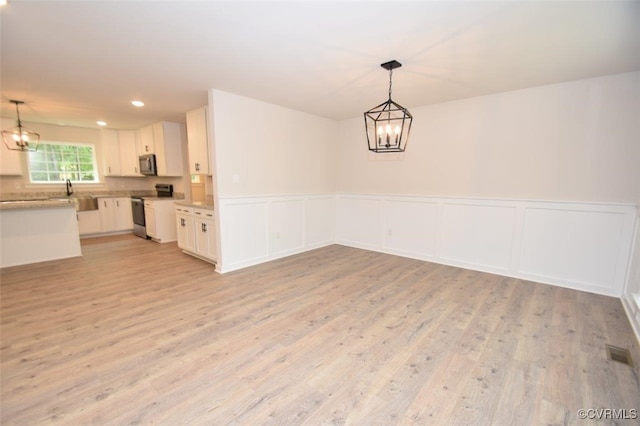 unfurnished dining area with visible vents, light wood-style flooring, wainscoting, and a notable chandelier