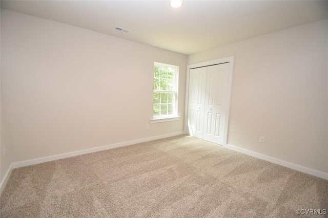 unfurnished bedroom featuring baseboards, visible vents, a closet, and light colored carpet
