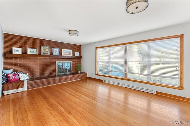 unfurnished living room featuring hardwood / wood-style flooring, brick wall, baseboard heating, and a brick fireplace