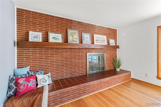 unfurnished living room with hardwood / wood-style flooring, a fireplace, and brick wall