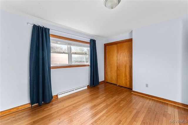 unfurnished room featuring a baseboard heating unit and light hardwood / wood-style floors