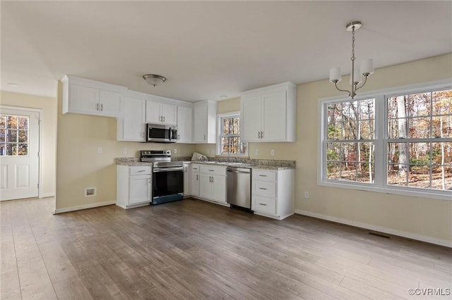 kitchen with white cabinetry, stainless steel appliances, light stone countertops, and hanging light fixtures