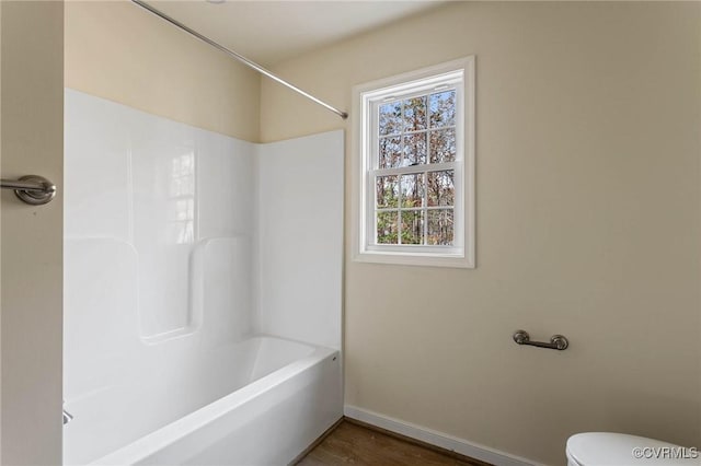 bathroom with hardwood / wood-style floors, shower / bathtub combination, and toilet