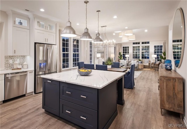 kitchen with appliances with stainless steel finishes, white cabinetry, a kitchen island, decorative light fixtures, and light wood-type flooring