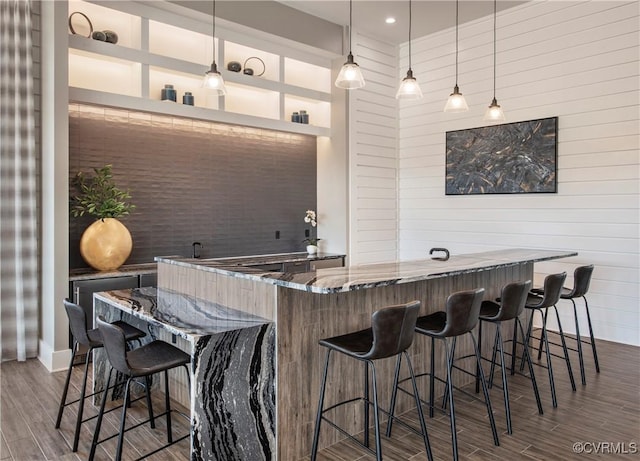 bar with hanging light fixtures, wood-type flooring, and stone counters