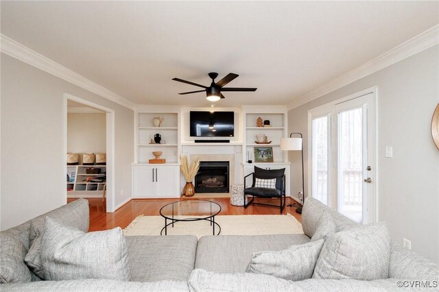 living room featuring crown molding, built in shelves, ceiling fan, and light wood-type flooring