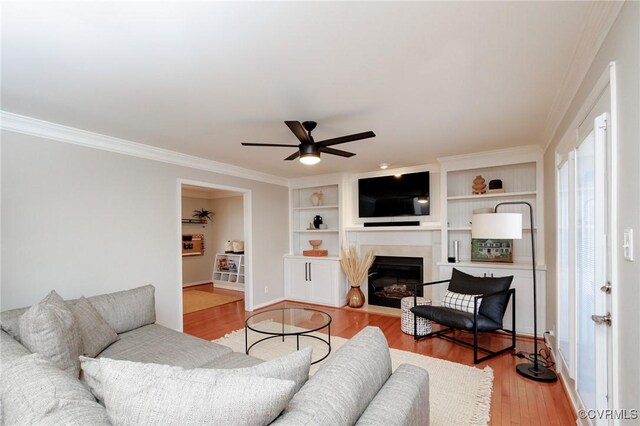 living room featuring crown molding, ceiling fan, light wood-type flooring, and built in shelves