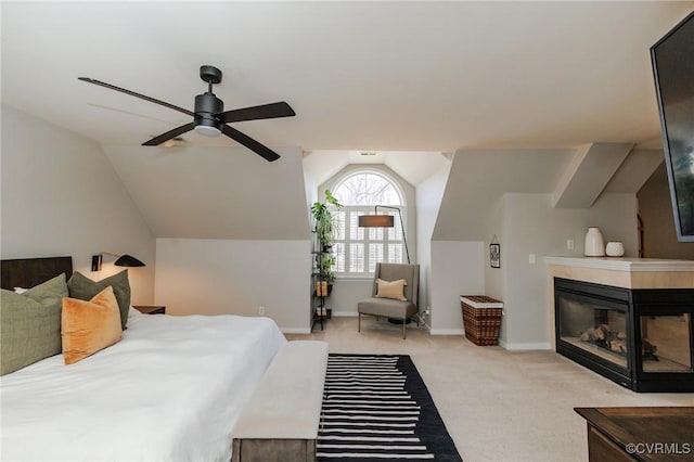 bedroom featuring light carpet, vaulted ceiling, a tile fireplace, and ceiling fan