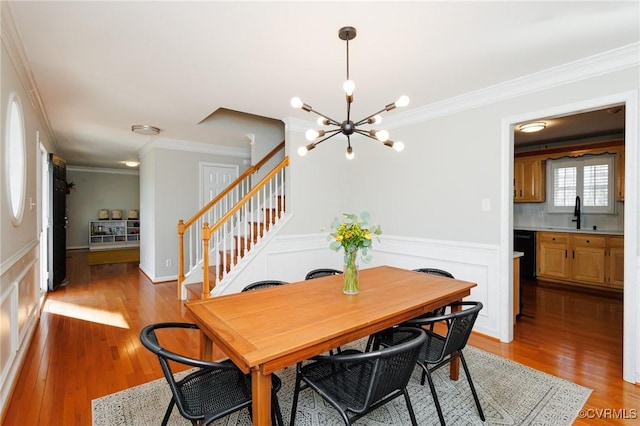 dining area with ornamental molding, sink, an inviting chandelier, and light hardwood / wood-style floors