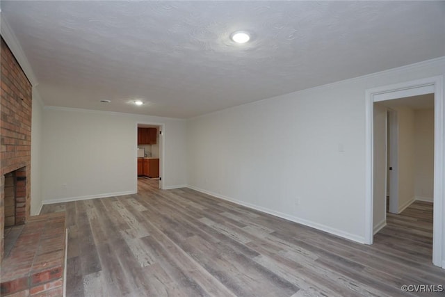 unfurnished living room featuring a brick fireplace, light hardwood / wood-style floors, a textured ceiling, and ornamental molding