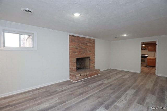 unfurnished living room featuring light wood-type flooring, ornamental molding, a brick fireplace, and a textured ceiling