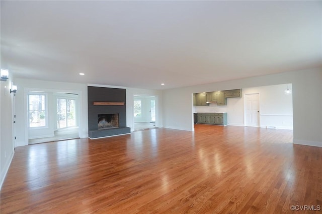 unfurnished living room featuring a brick fireplace, plenty of natural light, and wood-type flooring