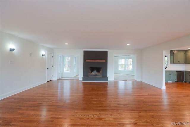 unfurnished living room with sink, a brick fireplace, and light hardwood / wood-style flooring