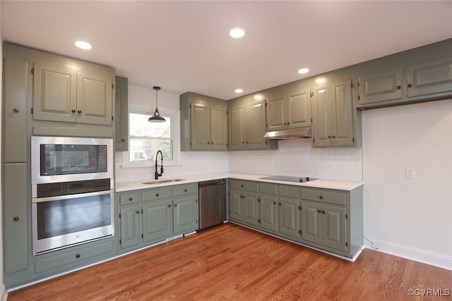 kitchen featuring appliances with stainless steel finishes, tasteful backsplash, light wood-type flooring, pendant lighting, and sink