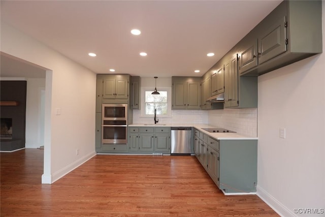 kitchen featuring stainless steel appliances, decorative backsplash, light hardwood / wood-style floors, decorative light fixtures, and sink