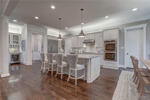 kitchen featuring light stone counters, appliances with stainless steel finishes, hanging light fixtures, and ornate columns