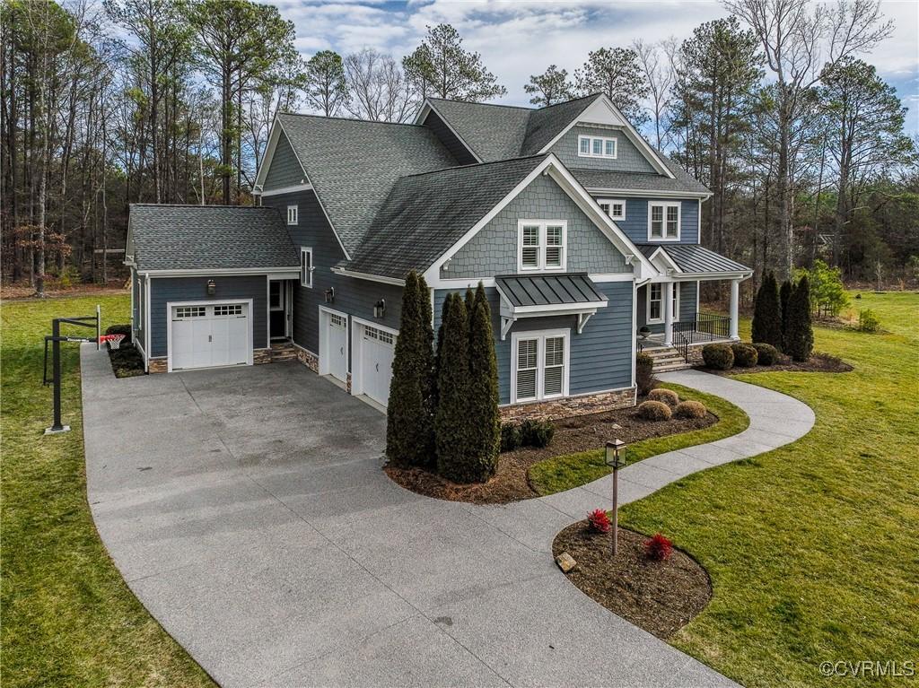 view of front of home featuring roof with shingles, an attached garage, stone siding, driveway, and a front yard