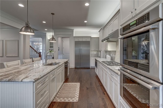 kitchen with pendant lighting, sink, crown molding, a kitchen island with sink, and stainless steel appliances