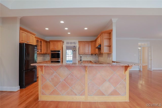 kitchen with black refrigerator, a breakfast bar, kitchen peninsula, crown molding, and light hardwood / wood-style flooring