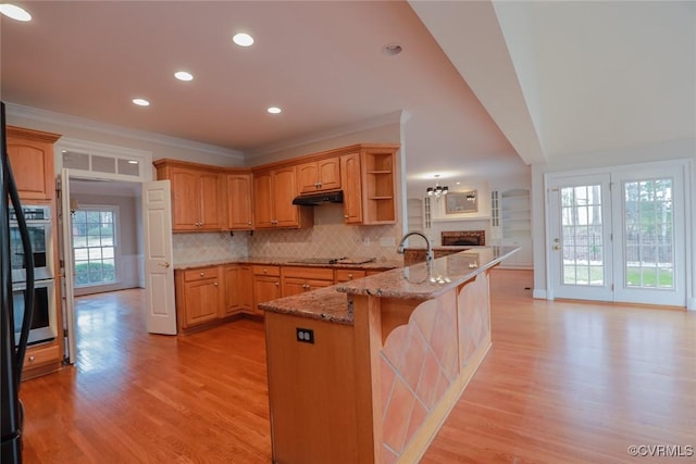 kitchen featuring a kitchen breakfast bar, decorative backsplash, ornamental molding, light stone counters, and light hardwood / wood-style floors