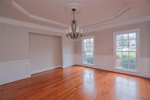 spare room featuring a raised ceiling, crown molding, hardwood / wood-style floors, and an inviting chandelier