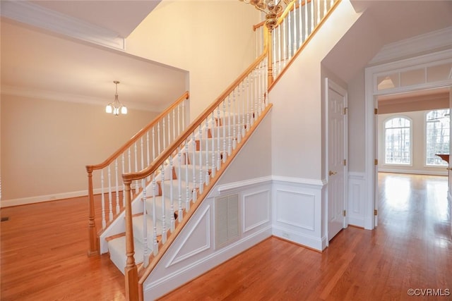 stairway with hardwood / wood-style flooring, crown molding, and a chandelier