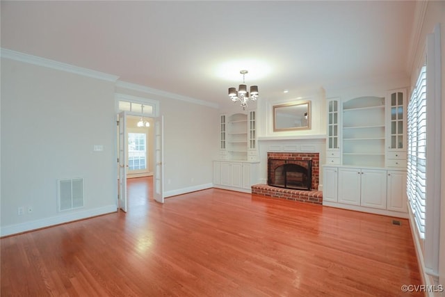 unfurnished living room with a brick fireplace, crown molding, a notable chandelier, and light wood-type flooring