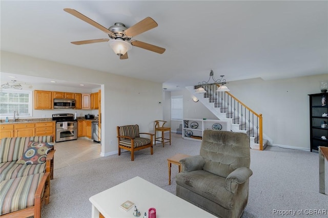 living area with baseboards, stairs, ceiling fan, and light colored carpet